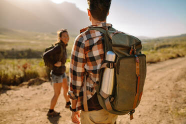 Rückansicht eines Mannes mit Rucksack beim Wandern in der Natur mit seiner Freundin im Hintergrund. Ein Paar beim Wandern in extremem Gelände. - JLPSF25701