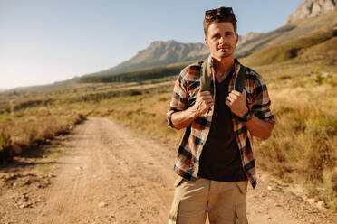 Porträt eines gutaussehenden Mannes mit Rucksack, der in der Natur wandert. Junger Wanderer auf einem Spaziergang an einem Sommertag. - JLPSF25706