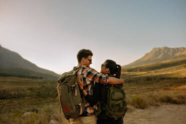 Rear view of young man and woman in love on hiking trip standing together. Loving couple on hiking trail in nature reserve. - JLPSF25708