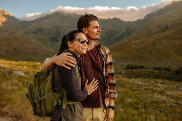 Aufnahme eines glücklichen jungen Paares auf einem Wanderausflug in der Natur, das die Aussicht bewundert. Junger Mann und Frau auf Wanderausflug stehen zusammen und betrachten die Aussicht. - JLPSF25710