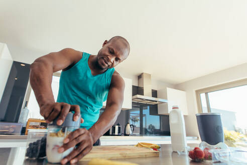 Ein Mann bereitet in der Küche einen Milchshake zu und gibt Früchte und Milch in einen Mixbehälter. - JLPSF25721