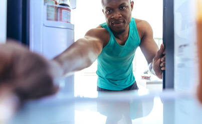 Mann, der zu Hause etwas in den Kühlschrank stellt. Fitnessbegeisterter, der nach dem Training einen Kühlschrank benutzt. - JLPSF25723