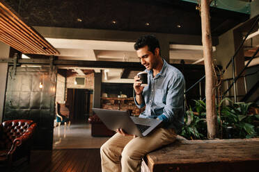 Aufnahme eines jungen Mannes, der entspannt am Laptop sitzt und Kaffee trinkt. Männliche Führungskraft, die in der Kaffeepause einen Laptop benutzt. - JLPSF25764