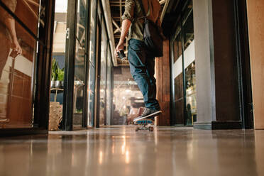 Low angle rear view shot of casual man skateboarding in office. Young businessman skating through his startup office. - JLPSF25795