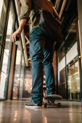 Rückansicht eines Mannes mit Skateboard im Büro. Junger Geschäftsmann fährt auf Skates durch den Bürokorridor. - JLPSF25796