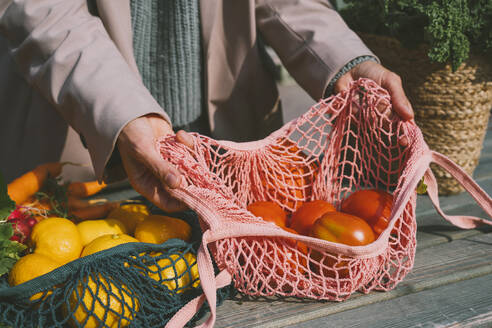 Hands of woman showing tomatoes in mesh bag on table - NDEF00038
