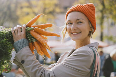 Happy woman holding bunch of carrots at market - NDEF00040