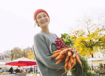 Happy woman holding organic vegetables at market - NDEF00048