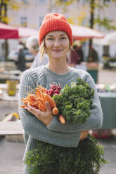 Smiling woman wearing sweater holding organic vegetables standing at market - NDEF00050