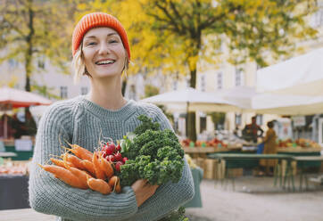 Glückliche Frau im Pullover mit Biogemüse auf dem Markt - NDEF00051