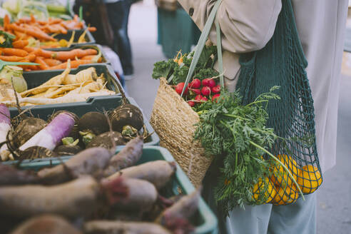 Woman holding shopping bags standing by vegetables in crate - NDEF00055