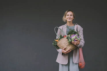 Smiling woman holding vegetable bags in front of gray wall - NDEF00063