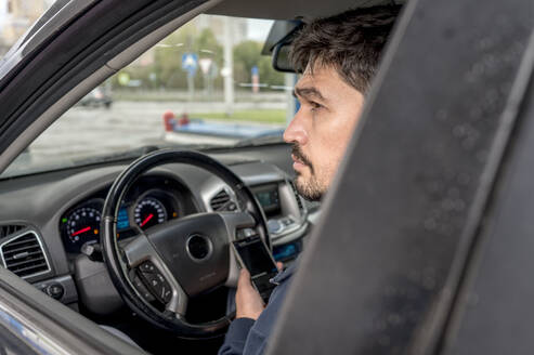 Nachdenklicher Mann mit Smartphone im Auto sitzend - ANAF00344