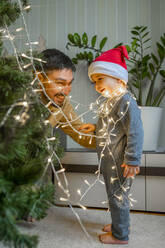 Niedlicher Junge mit Vater beim Schmücken des Weihnachtsbaums zu Hause - ANAF00351