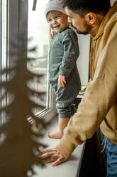 Sohn und Vater stehen am Fenster zu Hause - ANAF00357