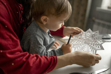 Mutter und Sohn basteln zu Hause Schneeflocken aus Papier - ANAF00363