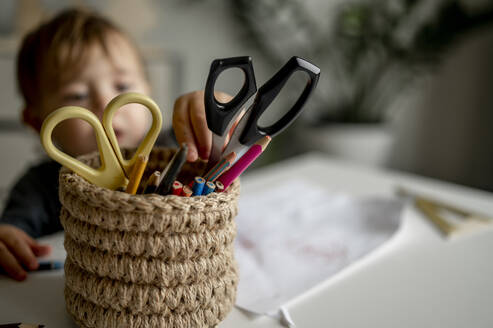 Boy picking up pencil from desk organizer at home - ANAF00387