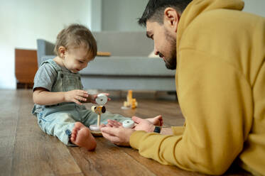 Father and son playing with wooden toy in living room - ANAF00391