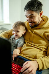 Glücklicher Vater und Sohn schauen auf den Laptop im Haus - ANAF00396