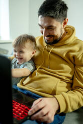 Glücklicher Vater sitzt mit seinem Sohn vor einem Laptop - ANAF00397
