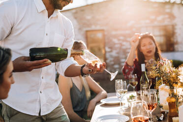 Mann serviert Freunden auf einer Party Champagner, Ausschnitt mit Fokus auf Hände, die Champagner in eine Flöte gießen. - JLPSF25813