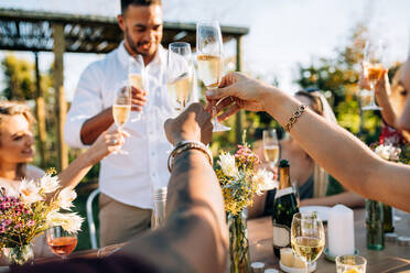 Eine Gruppe von Menschen stößt auf einer Party mit Getränken an. Junge Freunde trinken in einem Gartenrestaurant. - JLPSF25814