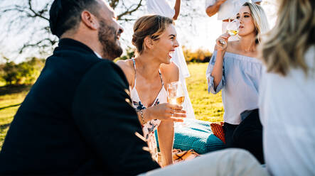 Junge, fröhliche Menschen, die im Gartenrestaurant sitzen und sich unterhalten und Wein trinken. - JLPSF25816