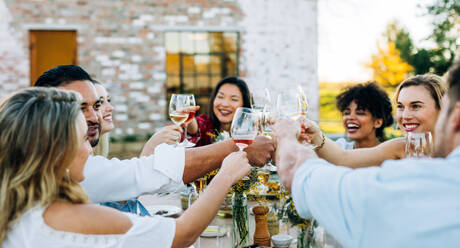 Eine Gruppe von Männern und Frauen stößt auf einer Party im Freien mit Wein an. Menschen trinken während des Mittagessens in einem Gartenrestaurant. - JLPSF25817