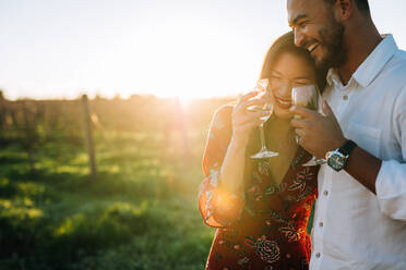 Paar, das mit einem Glas Wein im Freien spazieren geht. Mann und Frau mit einem Getränk in einem Weinberg. - JLPSF25819