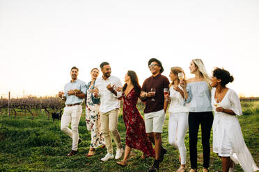 Group of friends chilling outside taking a walk together at vineyard. Men and woman with drinks walking outdoors. - JLPSF25820
