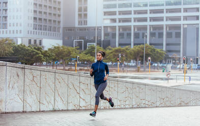 Läuferin im Jogging-Outfit, die auf einer Straße läuft. Frau hört Musik mit Kopfhörern beim Laufen. - JLPSF25831