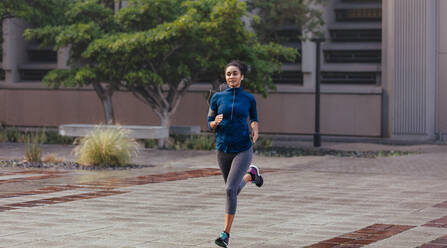 Frau hört Musik mit Kopfhörern beim Laufen. Läuferin im Jogging-Outfit läuft auf einer Straße. - JLPSF25832