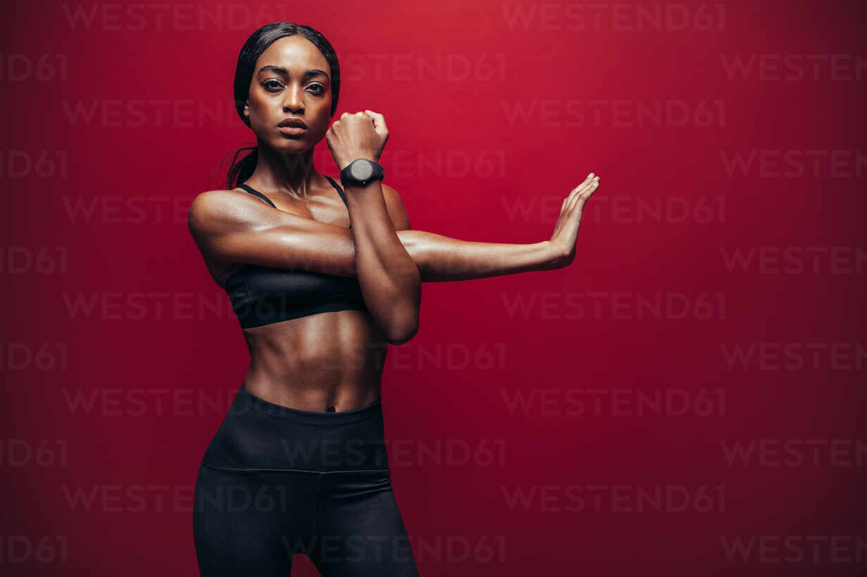 Fit woman doing exercise against red background. African female doing arm  stretching exercise to keep a good flexibility of her biceps. stock photo
