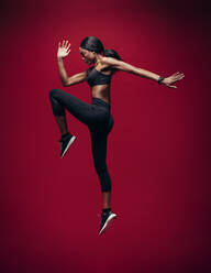 Sport Frau tun Springen und Stretching Workout. In voller Länge der gesunden jungen afrikanischen Fitness-Frau tun Übung über roten Hintergrund. - JLPSF25861