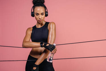 Fitness woman with headphones and water bottle leaning over rubber bands in studio. Female taking a break after exercising with resistance bands. - JLPSF25901