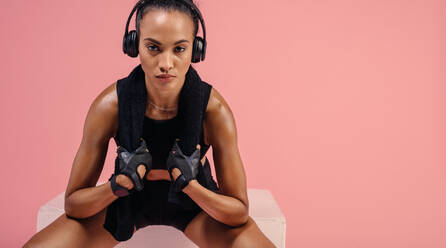 Woman with towel on neck and listening music on headphones. Strong young sports woman sitting after workout. - JLPSF25914