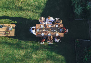 Luftaufnahme von Freunden, die eine Mahlzeit im Freien genießen. Eine Gruppe von Menschen sitzt um einen Tisch im Gartenrestaurant und isst gemeinsam. - JLPSF25933