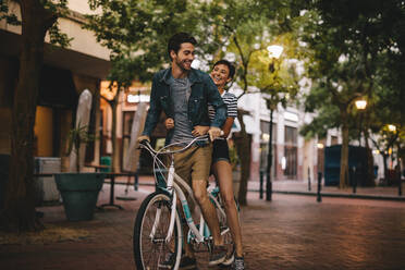 Verliebtes Paar auf dem Fahrrad in der Stadt. Mann fährt Fahrrad mit seiner Freundin auf dem Rücksitz. - JLPSF25938
