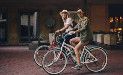 Freundinnen fahren mit ihren Fahrrädern auf einer Straße in der Stadt. Zwei Frauen genießen ihre Fahrradtour. - JLPSF25940