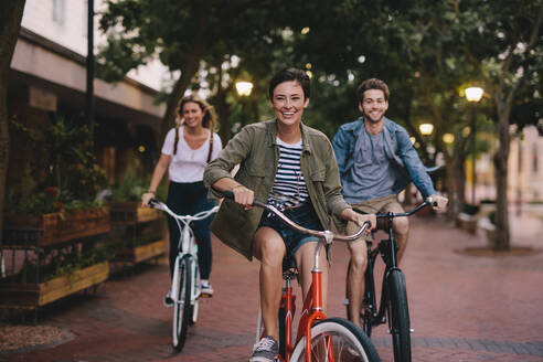 Drei junge Leute fahren mit dem Fahrrad die Straße hinunter, ein Mann und eine Frau sind mit ihren Fahrrädern unterwegs. - JLPSF25945