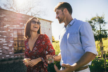 Multi-ethnic millennial couple walking outdoors and chatting. Man and woman with a drink at outdoors party. - JLPSF25966