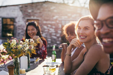 Beautiful young woman sitting at table with friends during a party. Multi-ethnic group of people having meal outdoors restaurant. - JLPSF25969