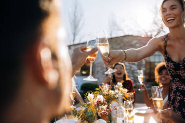 Lächelnde junge Frau stößt mit einem Freund auf einer Party im Freien mit Champagner an. Junge Leute genießen eine Party mit Fokus auf Champagnergläser. - JLPSF25980