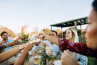 Eine Gruppe von Freunden stößt mit Weingläsern an und amüsiert sich im Freien. Menschen trinken beim Mittagessen im Gartenrestaurant. - JLPSF25985