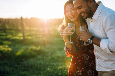 Paar mit einem Glas Wein und genießt die Gesellschaft des anderen. Mann und Frau mit einem Getränk und haben Spaß auf dem Weinberg. - JLPSF25990