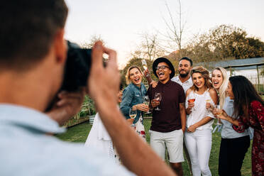 Man taking picture of his friends during a outdoor party. Group of people partying outdoors posing for a photograph at outdoor restaurant. - JLPSF25995