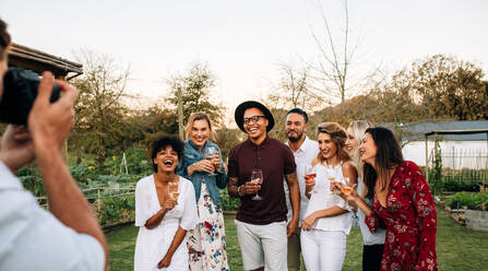 Eine Gruppe von Männern und Frauen posiert für ein Foto während einer Party im Freien. Ein Mann fotografiert seine Freunde bei einer Gartenparty. - JLPSF25996