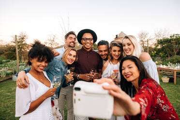 Woman with friends taking selfie using instant camera. Group selfie at outdoor party. - JLPSF25997