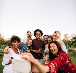 Eine Gruppe von Freunden macht ein Foto mit einer Sofortbildkamera. Männer und Frauen auf einer Gartenparty machen ein Selbstporträt. - JLPSF25998