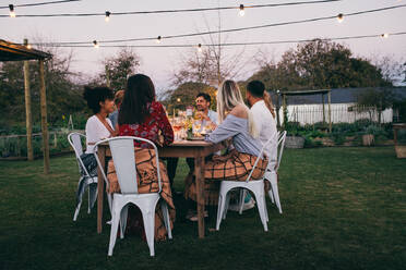 Eine Gruppe von Freunden sitzt in einem Restaurant im Freien und isst zu Abend. Junge Männer und Frauen feiern im Freien. - JLPSF25999